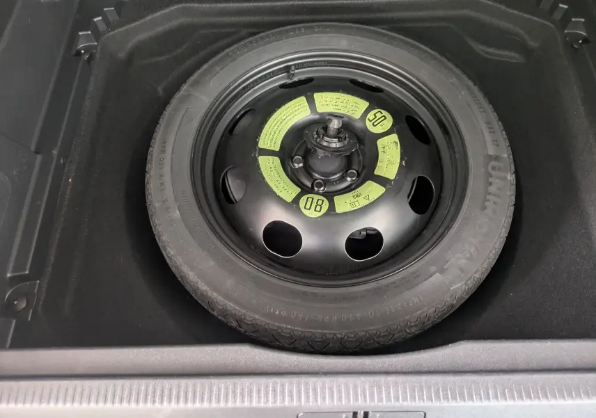 Roue de secours noire avec marquages jaunes, logée dans le coffre d'un Citroën C5 Aircross blanc.