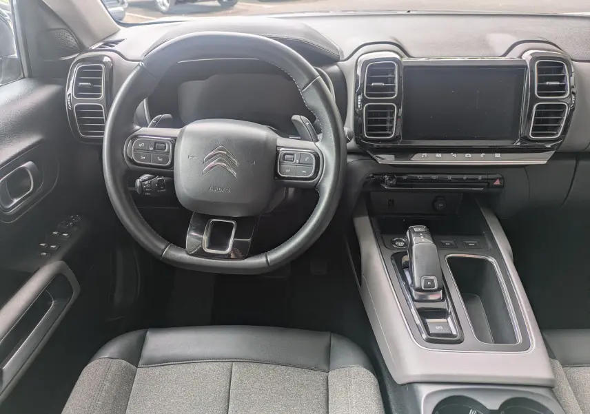 Vue intérieure frontale du poste de conduite du Citroën C5 Aircross blanc, avec volant multifonction et écran tactile central.