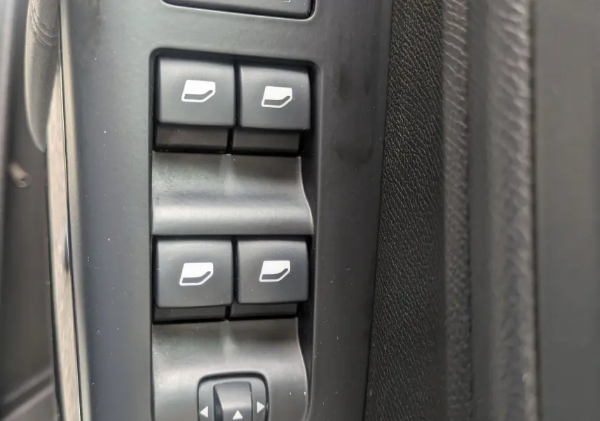 Vue rapprochée des commandes de lève-vitres et réglages des rétroviseurs sur la porte côté conducteur d'un Citroën C5 Aircross blanc.