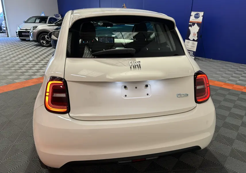 Vue arrière d'une FIAT 500 électrique blanche 2023 avec feux arrière allumés en intérieur showroom.