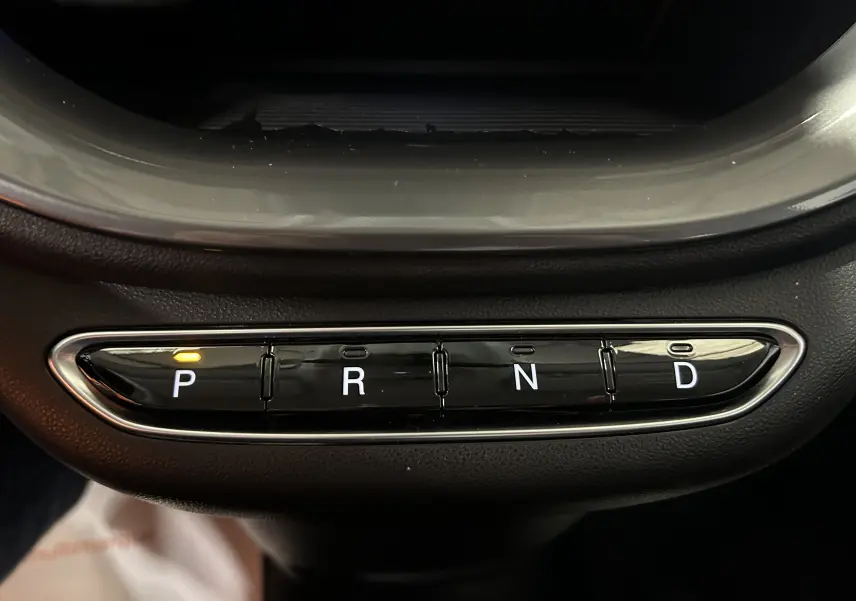 Gros plan sur la commande de boîte automatique noire avec boutons P, R, N, D et témoin lumineux orange sur P.