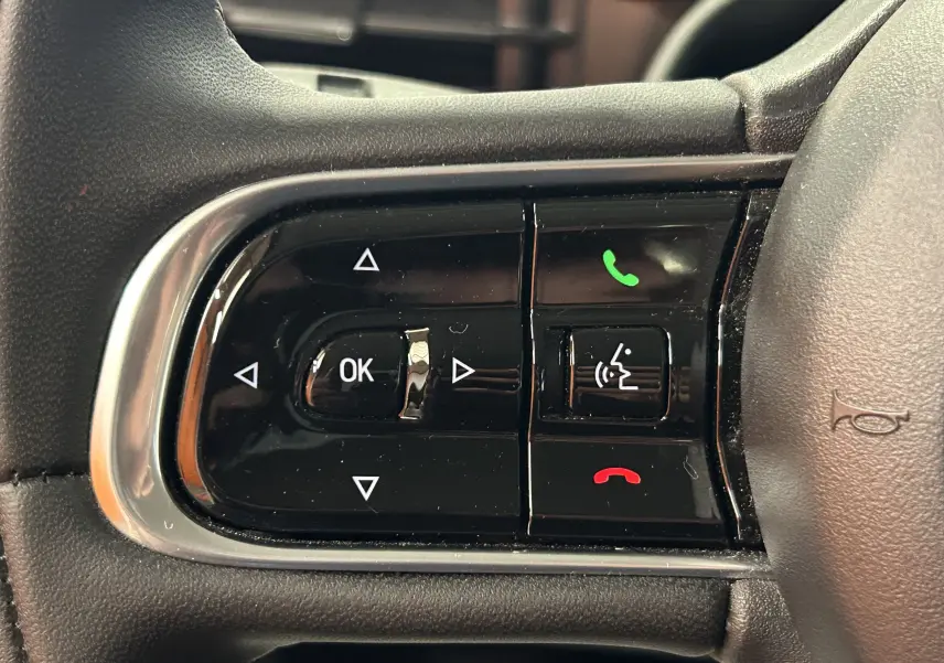 Gros plan sur les commandes multifonctions noires à gauche du volant d’un Fiat 500 électrique blanc, avec boutons appel et navigation.