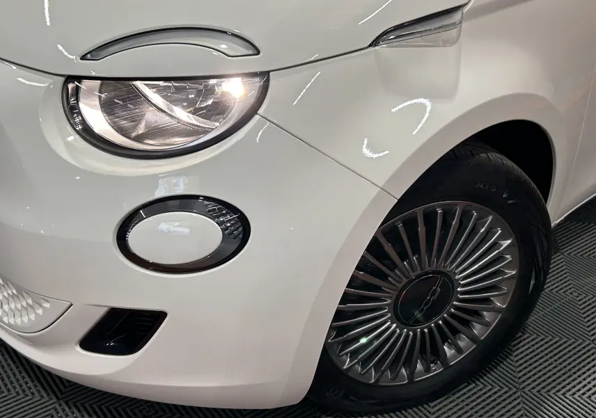 Gros plan sur l’avant droit blanc du FIAT 500 électrique 2023, mettant en valeur le phare et la jante stylisée.