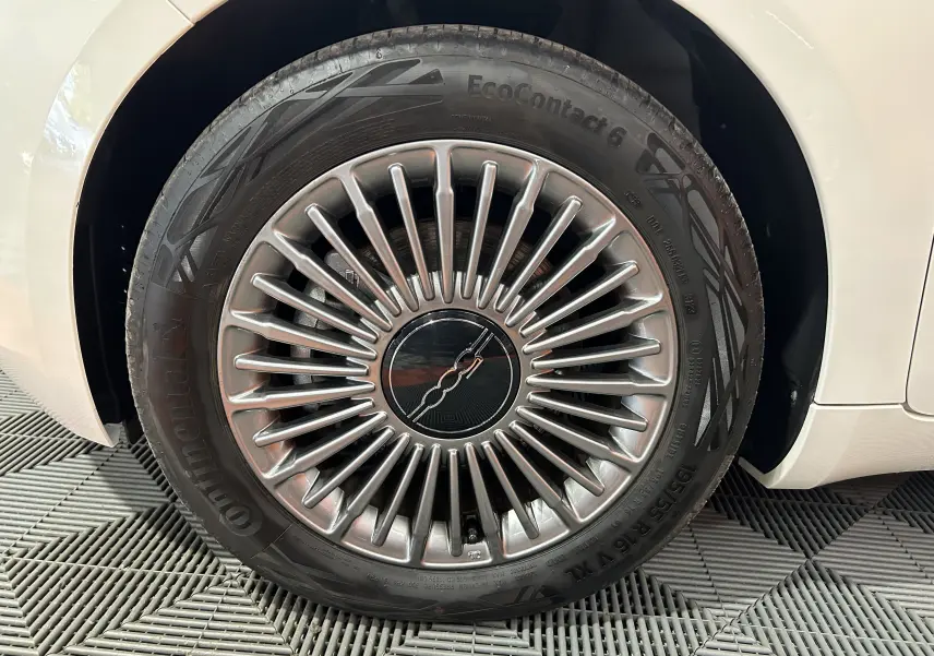 Gros plan sur la roue avant droite d'une FIAT 500 électrique blanche, mettant en valeur la jante argentée au design rayonné.