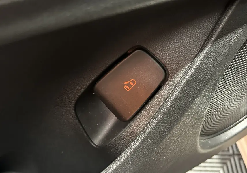 Gros plan sur le bouton de verrouillage des portes orange dans l'habitacle noir d'une Fiat 500 électrique blanche.