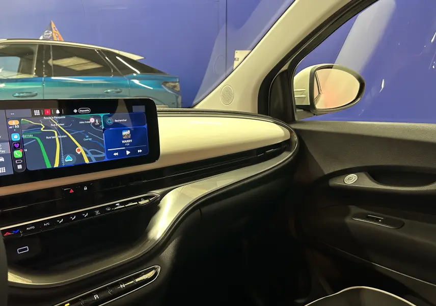 Intérieur côté passager de la Fiat 500 électrique blanche 2023, avec tableau de bord épuré et écran tactile central allumé.