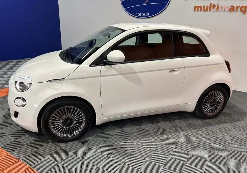 Vue de profil côté gauche d'une Fiat 500 électrique blanche 2023 avec jantes spécifiques et vitres teintées.