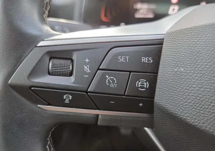 Gros plan sur les commandes multifonctions du volant de la SEAT IBIZA 2025, boutons noirs avec symboles blancs.