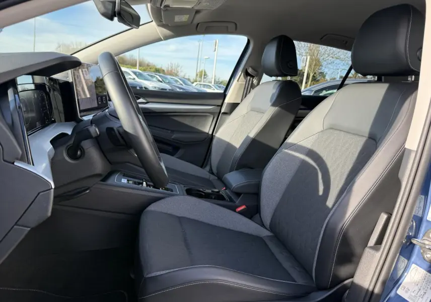 Vue intérieure côté conducteur de la Volkswagen Golf 2025 bleu anémone, avec sièges tissu et cuir gris et volant multifonction.