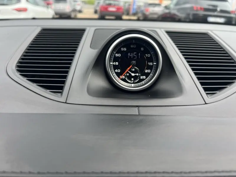 Gros plan sur l'horloge centrale noire du tableau de bord du Porsche Macan 2018, entourée de grilles d'aération noires.
