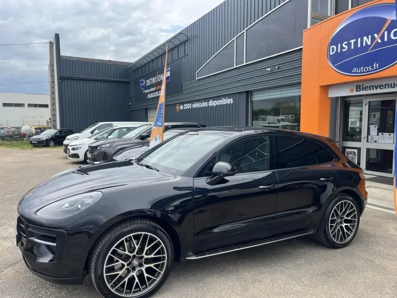 Porsche Macan noir en 3/4 avant droit, avec jantes sport 21 pouces et vitres teintées, stationné devant un garage.