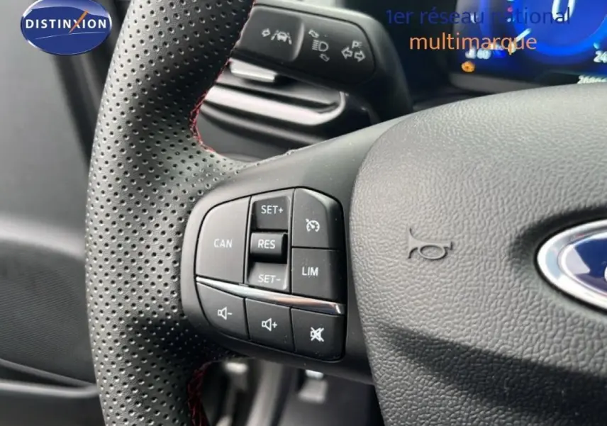 Gros plan sur le volant perforé gris foncé du Ford Puma 2024 avec commandes de régulateur et volume audio.