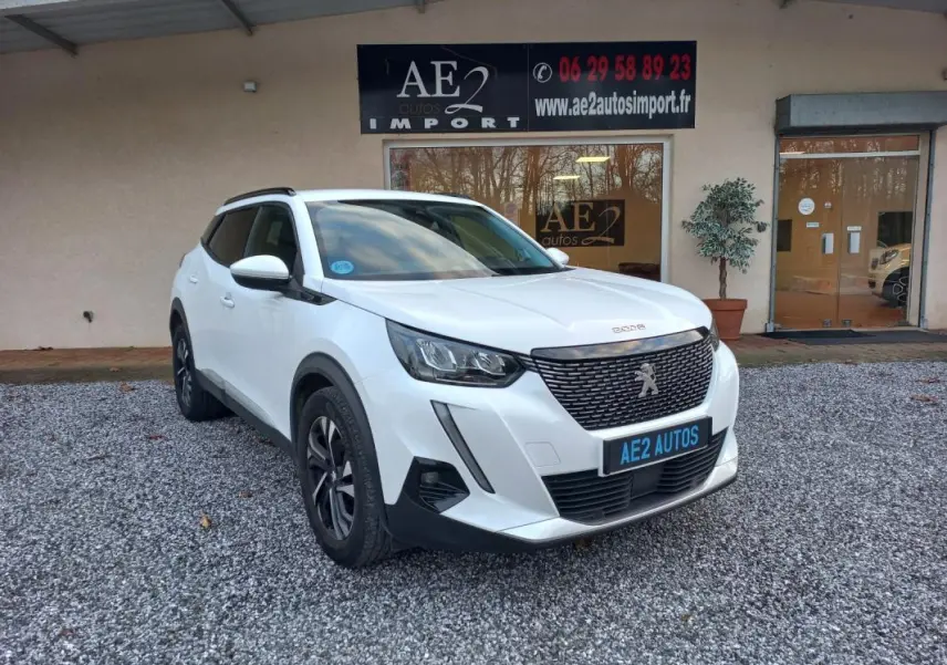 Peugeot 2008 blanc vue 3/4 avant droit, avec calandre noire et jantes alliage, stationné devant un bâtiment.