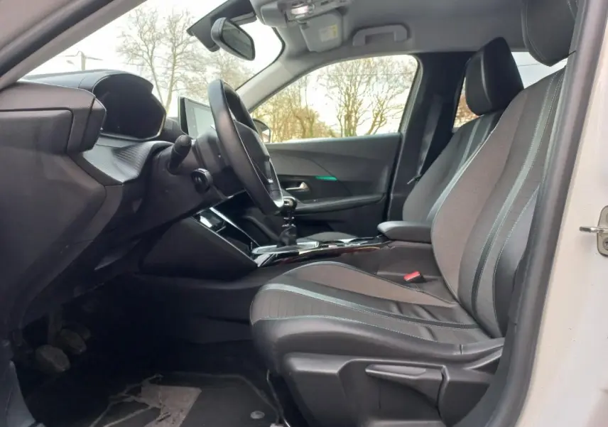 Vue intérieure côté conducteur de la Peugeot 2008 blanche 2021, montrant les sièges et le tableau de bord moderne.