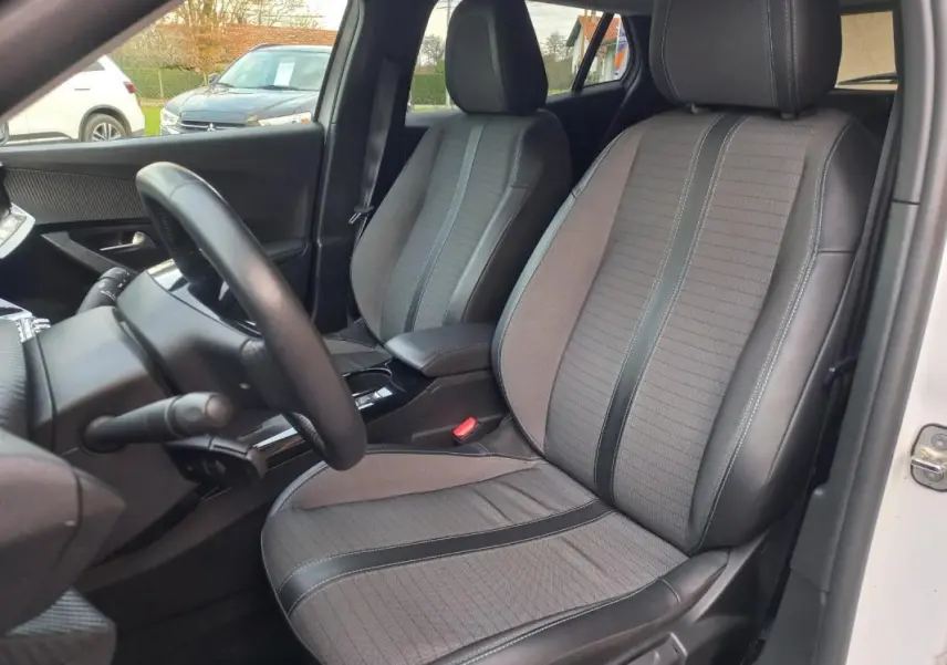 Vue intérieure côté conducteur du Peugeot 2008 blanc 2021, sièges tissu gris avec inserts noirs et volant visible.