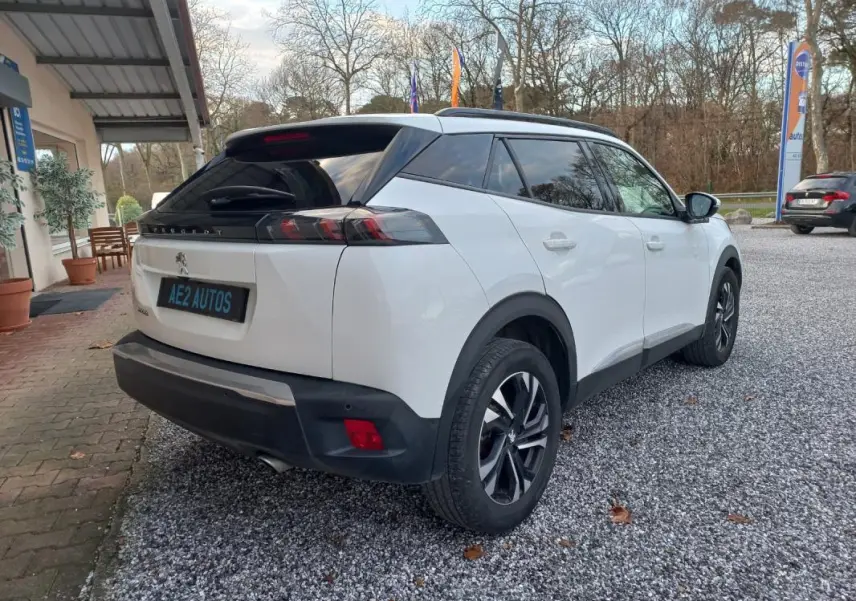 Peugeot 2008 blanc vue 3/4 arrière droit avec jantes alliage et toit noir dans un parking extérieur.