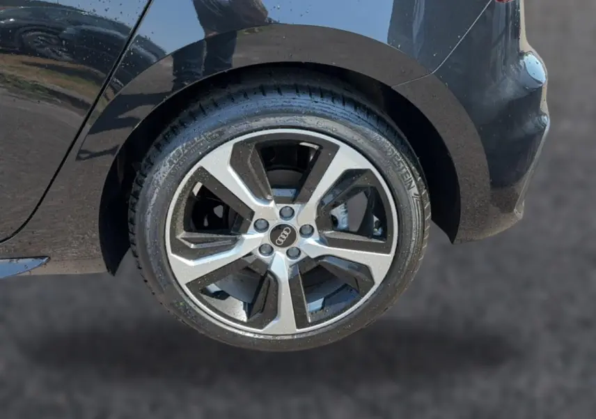 Gros plan sur la roue arrière droite d'une Audi A1 Sportback noire, mettant en valeur la jante alu au design moderne.