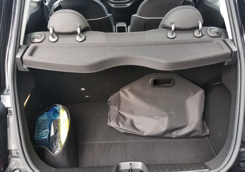 Vue arrière du coffre ouvert d'une FIAT 500 électrique noire 2024, avec housse et rangement latéral visible.