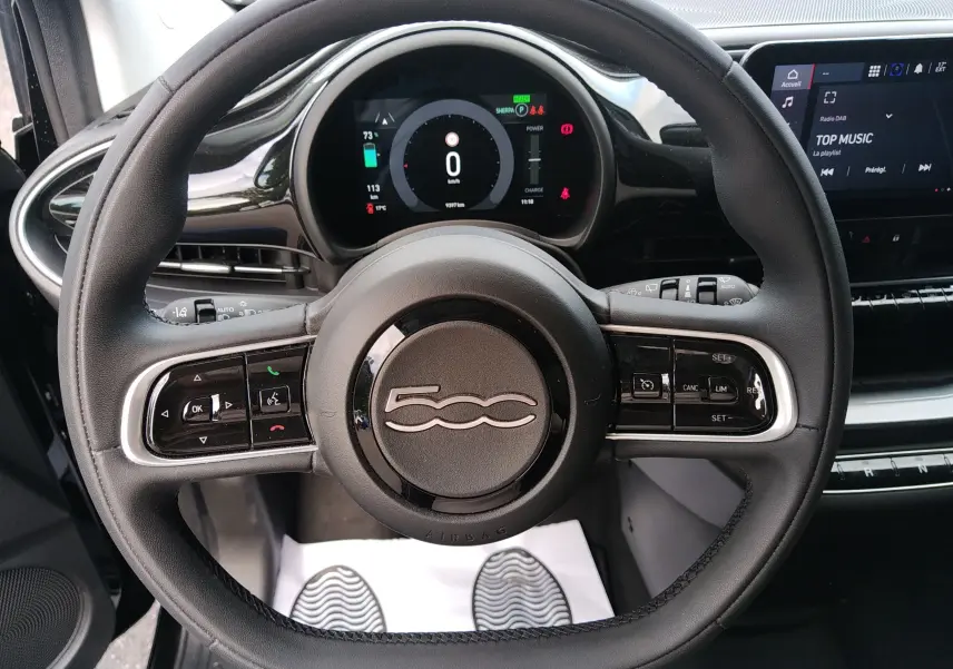 Vue intérieure centrée sur le volant noir de la Fiat 500 électrique 2024 avec tableau de bord digital et écran tactile.