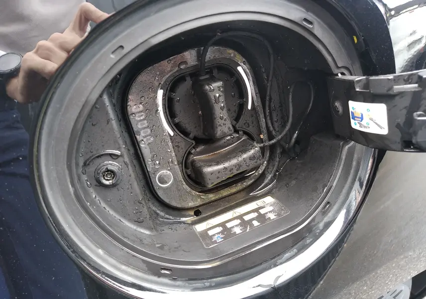 Gros plan sur la trappe de recharge électrique ouverte d'une FIAT 500 noire, avec connecteur visible et gouttes d'eau.