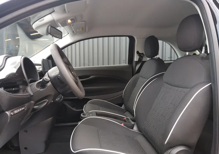 Vue intérieure côté conducteur de la Fiat 500 électrique 2024, sièges noirs avec surpiqûres blanches et volant multifonction.