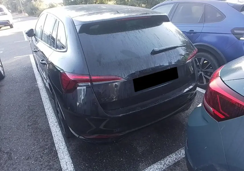 Vue 3/4 arrière d'une Skoda Scala noire Magic avec hayon électrique, stationnée entre deux véhicules.