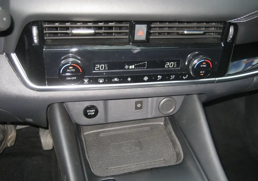 Console centrale du Nissan Qashqai 2024 montrant la commande de climatisation digitale et le bouton start/stop noir.