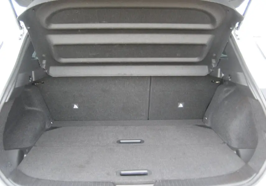 Coffre ouvert d'un Nissan Qashqai blanc 2024, vue arrière montrant l'espace de chargement vide et la moquette grise.