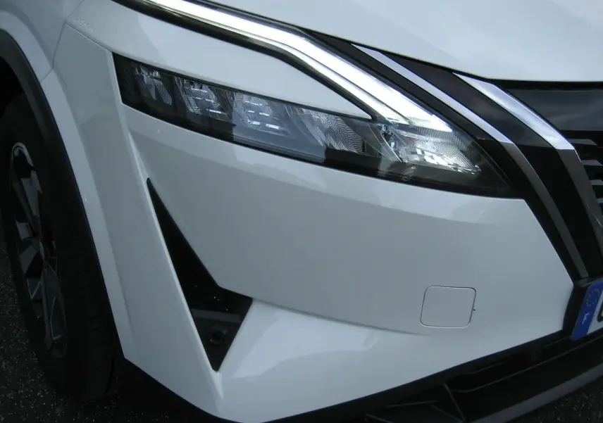 Gros plan sur l'avant gauche blanc du Nissan Qashqai 2024, mettant en valeur le phare LED et la calandre noire.