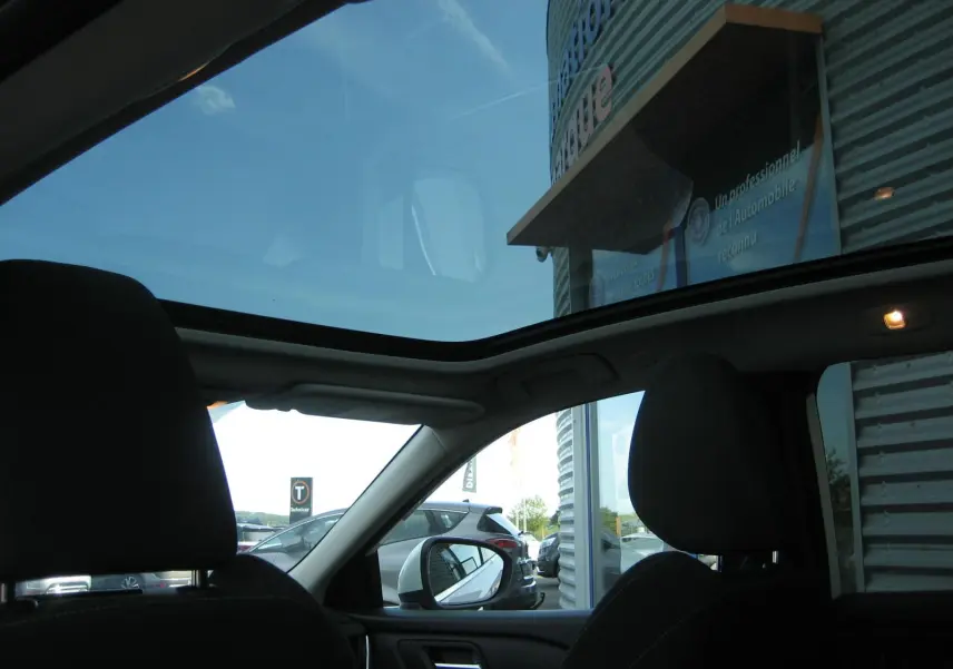 Vue intérieure du Nissan Qashqai blanc 2024 montrant le toit panoramique et les sièges avant noirs.
