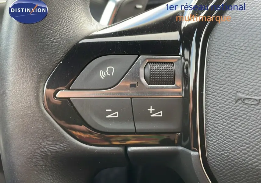 Gros plan sur les commandes de volume et de voix au volant cuir noir de la Peugeot 508 Gris Platinium 2023.