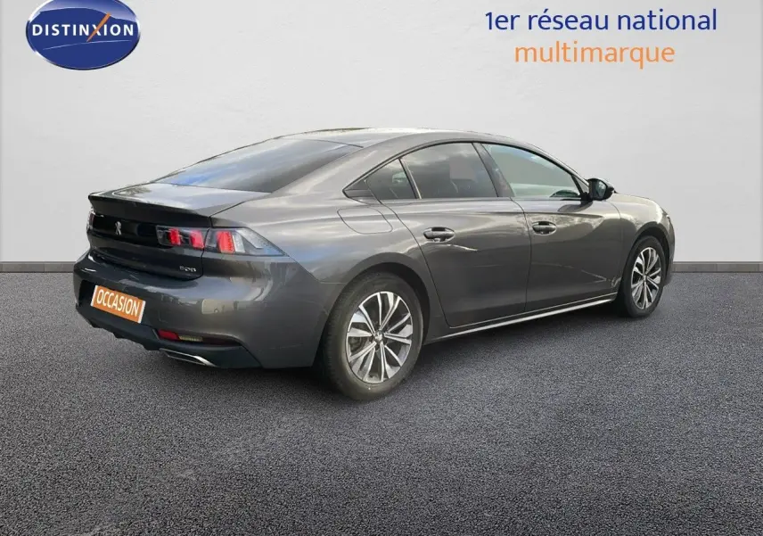 Peugeot 508 gris platinium métal vue 3/4 arrière côté droit sur sol gris avec logo Distinxion en arrière-plan.