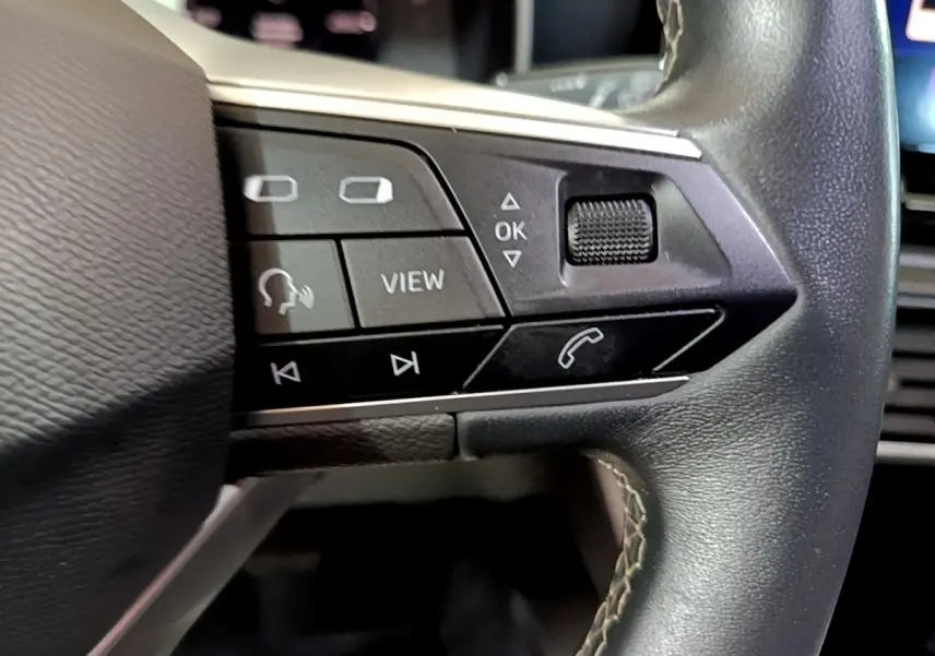 Gros plan sur les commandes gauche du volant cuir du SEAT LEON gris clair 2022, avec boutons multifonctions et molette.