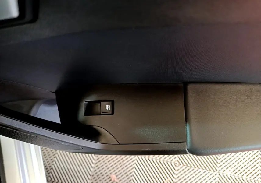 Bouton de commande de lève-vitre arrière droit noir sur panneau de porte intérieur gris foncé d'une SEAT Leon 2022.
