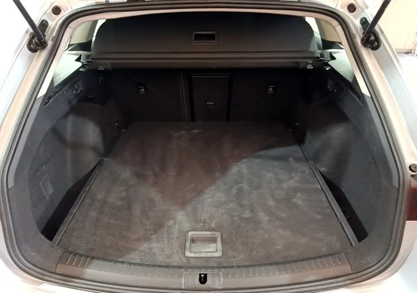 Coffre ouvert vu de l'arrière d'une SEAT LEON gris clair, espace de chargement spacieux et tapis noir.