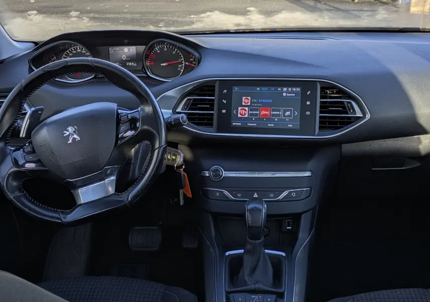 Vue intérieure avant de la Peugeot 308 SW noire, montrant le tableau de bord avec écran tactile et volant cuir.