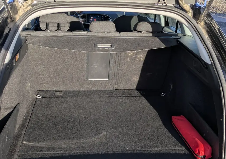 Coffre ouvert d'une Peugeot 308 SW noire, vue arrière montrant l'espace de chargement et un triangle de sécurité rouge.