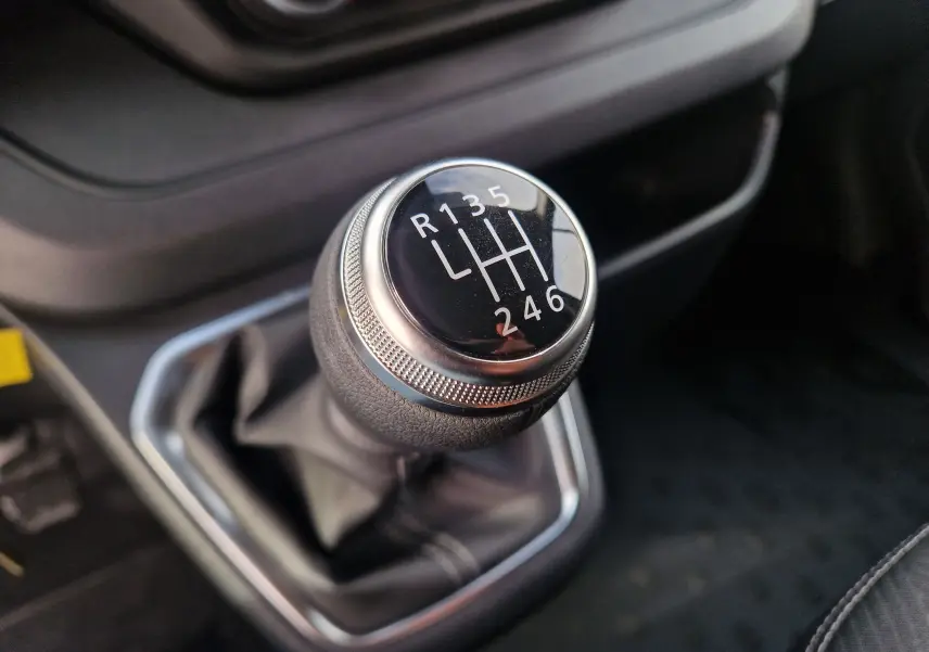 Gros plan sur le levier de vitesses manuel noir du Nissan Primastar 2025 avec marquages blancs et contour chromé.