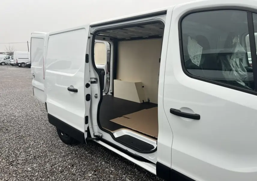 Vue 3/4 arrière droite d'un utilitaire Nissan Primastar blanc, avec portes arrière fermées sur un terrain extérieur.