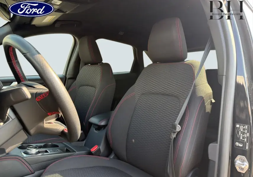 Vue intérieure avant droite du Ford Kuga 2025 noir Agate, sièges tissu ST-Line avec surpiqûres rouges et volant multifonction.