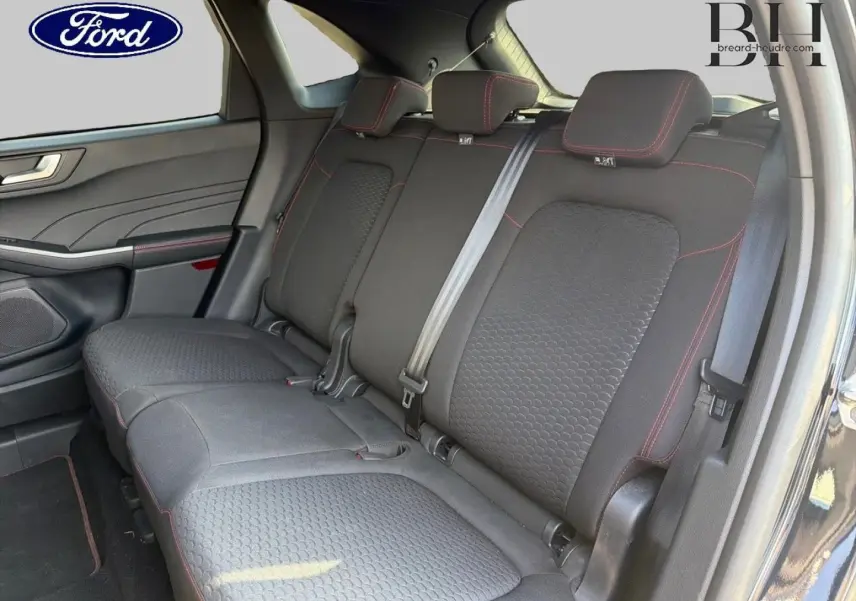 Vue intérieure du Ford Kuga 2025 montrant la banquette arrière en tissu noir avec surpiqûres rouges et ceintures grises.