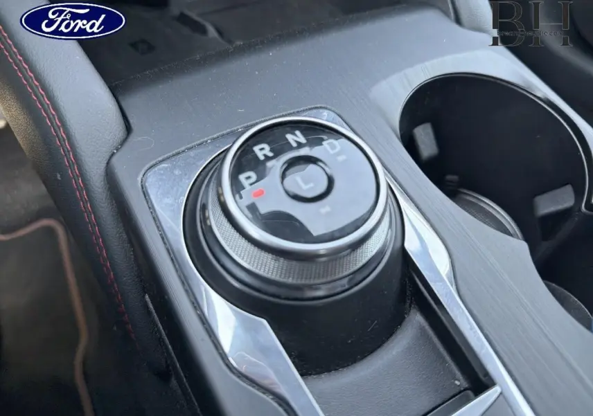 Gros plan sur la molette de sélection de la boîte automatique du Ford Kuga noir avec surpiqûres rouges, console centrale visible.