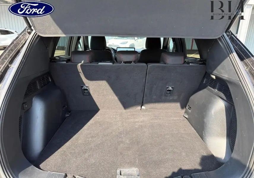 Coffre ouvert vu de l'arrière du Ford Kuga 2025, montrant un espace de chargement spacieux et tapis noir.