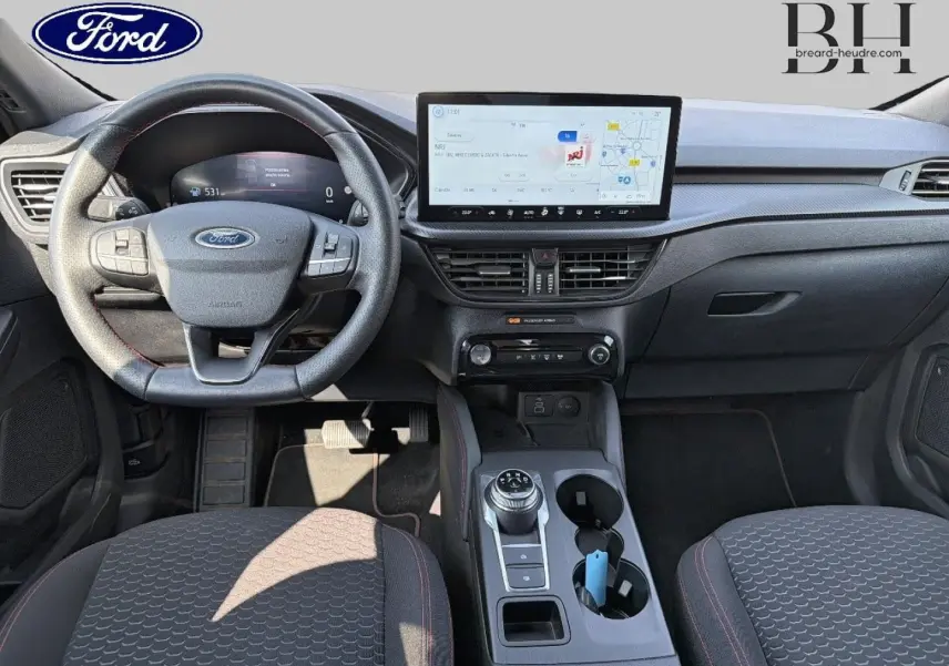 Vue intérieure avant du Ford Kuga 2025, tableau de bord noir avec écran tactile large et volant multifonction.