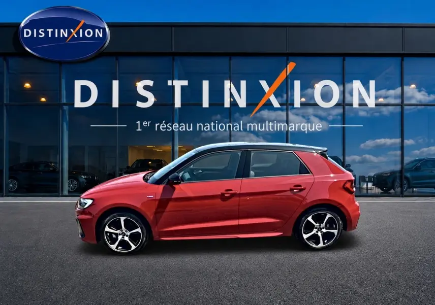 Profil droit d'une Audi A1 Sportback 30 TFSI rouge toit noir avec jantes alu et becquet arrière, devant une vitrine Distinxion.
