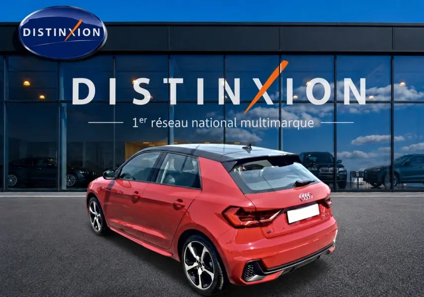 Audi A1 Sportback rouge et noir vue 3/4 arrière droit, avec jantes alu et toit contrasté noir devant vitrine Distinxion.
