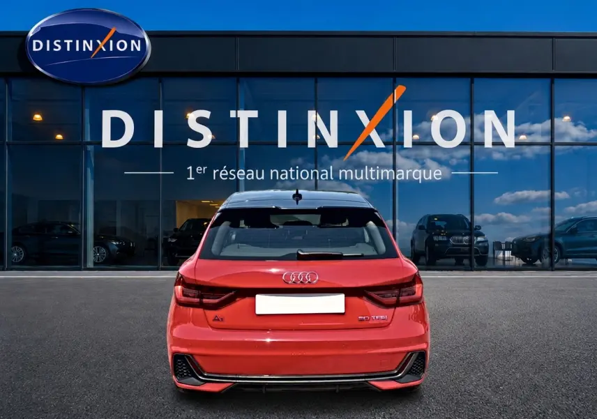Vue arrière d'une Audi A1 Sportback 30 TFSI rouge et noir, avec becquet et feux arrière LED, devant une vitrine Distinxion.