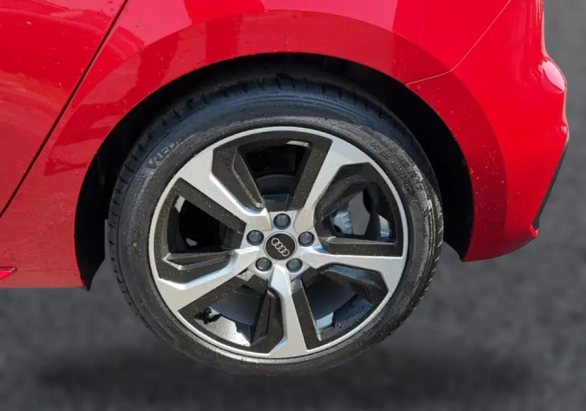 Gros plan sur la roue arrière droite d'une Audi A1 Sportback rouge, mettant en valeur la jante alu bicolore et le logo Audi.