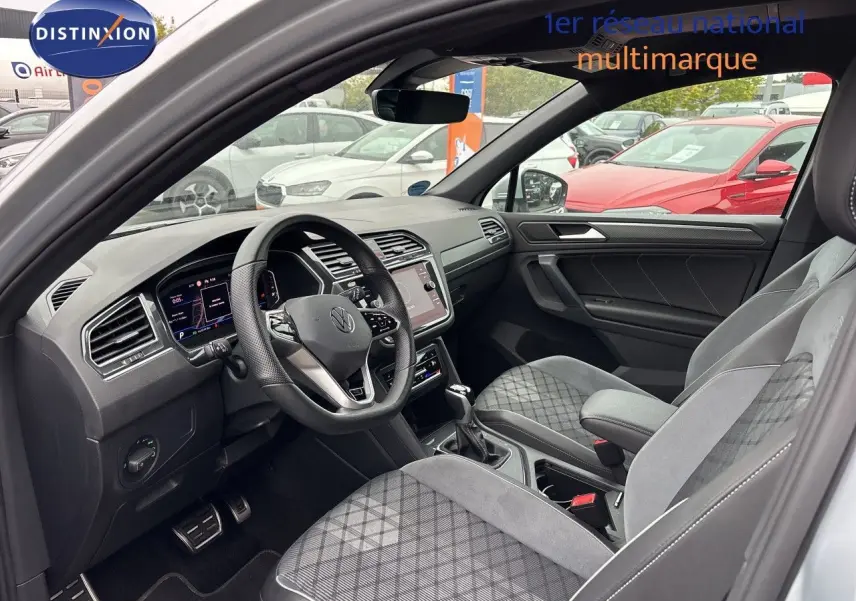Vue intérieure côté conducteur du Volkswagen Tiguan 2024, montrant le tableau de bord moderne et les sièges gris/noir en tissu et cuir.