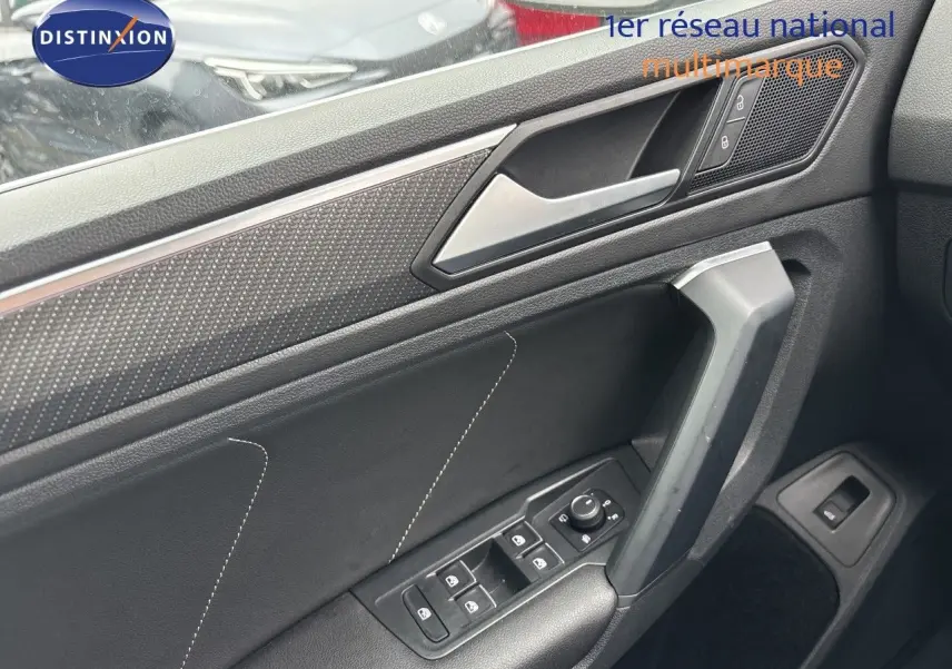 Détail de la porte avant gauche du Volkswagen Tiguan 2024 en intérieur noir avec commandes des vitres et poignée angulaire.